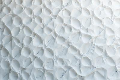 The primary subject of the image is a large, white marble wall with a pattern of white circles. The setting is a room with a white marble surface, which creates a clean and elegant atmosphere. The visual style is a combination of a photo and digital art, as the circles are arranged in a visually appealing manner. The colors and mood of the image are predominantly white, giving it a calm and serene appearance.