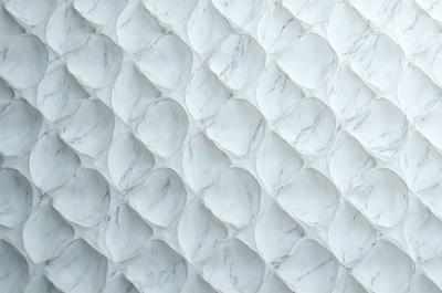 The primary subject of the image is a white marble wall with a pattern of circles. The setting is a white marble wall, and the visual style is a photo. The dominant colors are white and gray, creating a clean and elegant atmosphere.