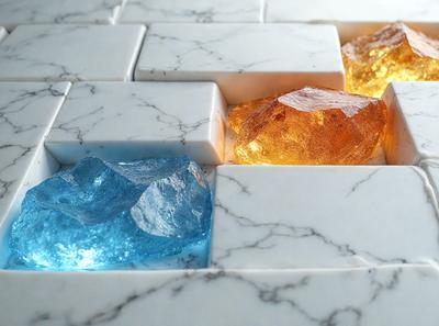 The primary subject of the image is a marble tiled surface with a variety of colored rocks placed on it. The setting is a white marble countertop, and the visual style is a close-up of the rocks on the marble. The colors and mood of the image are vibrant and lively, with the rocks in various shades of blue, yellow, and orange.