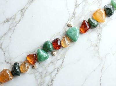 The primary subject of the image is a row of colorful rocks, including a mix of green, orange, and red, arranged on a marble countertop. The setting is a white marble countertop, which serves as the background for the scene. The visual style of the image is a close-up of the rocks, showcasing their vibrant colors and unique shapes. The overall atmosphere of the image is lively and visually appealing, with the rocks creating a striking pattern on the marble surface.