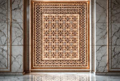 The primary subject of the image is a decorative wooden door with a patterned design. The door is adorned with a beautifully crafted wooden design, which adds a touch of elegance to the scene. The setting is a room with a marble floor, which complements the door's design. The visual style of the image is a close-up of the door, showcasing its intricate details. The colors and mood of the image are warm and inviting, with the wooden door and marble floor creating