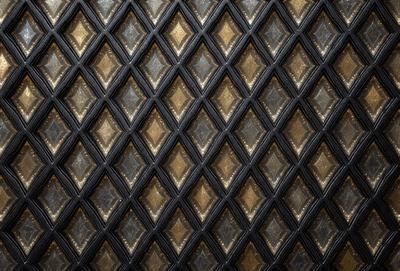 The primary subject of the image is a close-up of a patterned surface, which appears to be a black and gold design. The setting is a black and gold wall, and the visual style is a close-up of the pattern. The colors and mood of the image are predominantly black and gold, creating a sophisticated and elegant atmosphere.