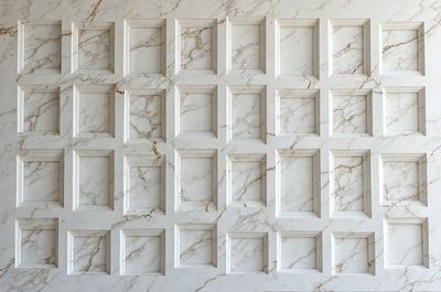 The primary subject of the image is a white marble wall with a pattern of square tiles. The setting is a room with a white marble wall, and the visual style is a photo. The dominant colors are white and gray, creating a clean and elegant atmosphere.