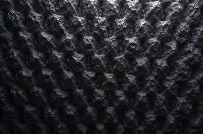 The primary subject of the image is a close-up of a rocky surface with a pattern of holes and ridges. The setting is a dark, possibly underground environment. The visual style is a combination of a photo and digital art, creating a unique and intriguing appearance. The dominant colors are black and grey, giving the image a moody and mysterious atmosphere.