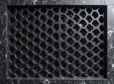 The primary subject of the image is a black and white patterned grate. The setting is a black background, which contrasts with the patterned grate. The visual style is a close-up of the grate, showcasing its intricate design. The colors and mood of the image are predominantly black and white, giving it a classic and timeless appearance.