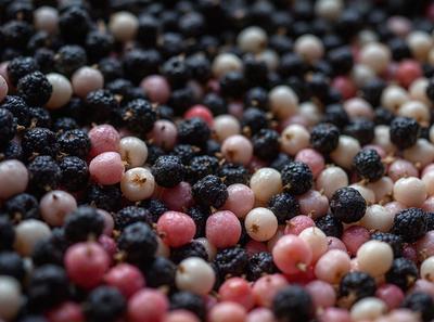 The primary subject of the image is a close-up of a pile of blackberries, raspberries, and cherries. The setting is a table with a patterned surface, and the visual style is a close-up of the fruits. The colors and mood of the image are predominantly dark, with the blackberries, raspberries, and cherries being the main focus.