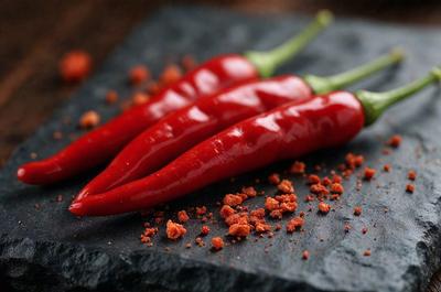 The primary subject of the image is a pair of red peppers, which are the main objects in the scene. They are placed on a black surface, which serves as the background. The visual style of the image is a photo, capturing the vibrant colors and details of the peppers. The dominant colors in the image are red and black, creating a bold and striking appearance.