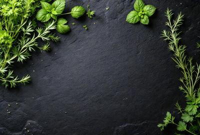 The primary subject of the image is a black slate surface with green mint leaves and stems scattered across it. The setting is a kitchen counter, and the visual style is a close-up of the mint leaves. The dominant colors are black and green, creating a natural and fresh atmosphere.