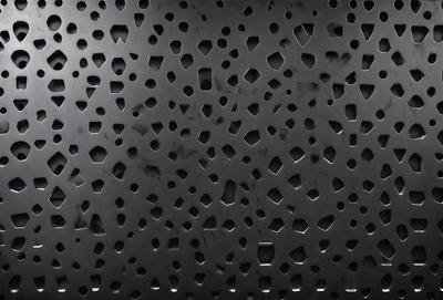 The primary subject of the image is a black surface with a pattern of small holes. The setting is a black background, and the visual style appears to be a pattern or texture. The dominant colors are black and white, and the overall atmosphere is somewhat mysterious or intriguing.