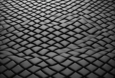 The primary subject of the image is a black, textured surface with a pattern resembling a fish scale. The setting is a black background, and the visual style appears to be a close-up of the textured surface. The colors and mood of the image are predominantly dark and moody, with the black background and textured surface creating a sense of depth and intrigue.