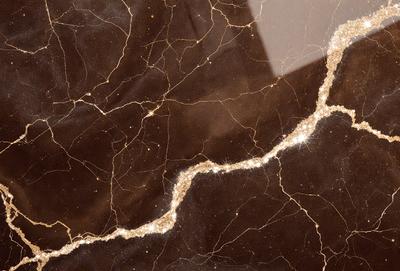 The primary subject of the image is a marble countertop with a gold vein running through it. The setting is a kitchen, and the visual style is a close-up of the marble countertop. The colors and mood of the image are warm and luxurious, with the gold vein adding a touch of elegance to the marble surface.