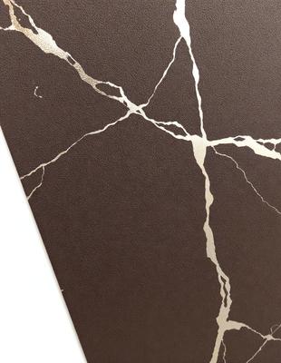 The primary subject of the image is a brown leather book with a gold design on the cover. The setting is a white background, which contrasts with the brown leather and gold design. The visual style is a combination of a photo and digital art, as the gold design appears to be a digital element added to the leather book. The colors and mood of the image are warm and elegant, with the brown leather and gold design creating a sense of sophistication and luxury.