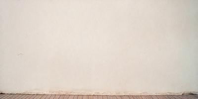 The primary subject of the image is a white wall with a large, empty space. The setting is a room with a wooden floor. The visual style is a photo, and the colors and mood are predominantly white, giving the image a clean and minimalist appearance.
