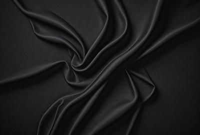 The primary subject of the image is a close-up of a black fabric, possibly a piece of clothing or a curtain. The setting is a dark background, which emphasizes the fabric's texture and pattern. The visual style appears to be a photo, as it captures the details of the fabric. The colors and mood of the image are predominantly dark, with the black fabric being the main focus.
