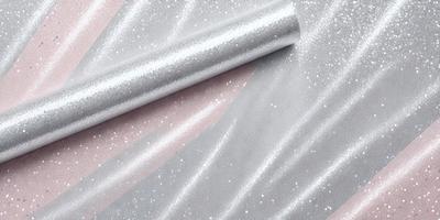 The primary subject of the image is a silver metallic material, possibly a piece of fabric or a metal sheet, with a glittery texture. The setting is a pink background, which contrasts with the silver material. The visual style appears to be a close-up of the silver material, showcasing its unique texture and appearance. The colors and mood of the image are predominantly silver and pink, creating a visually appealing and contrasting scene.