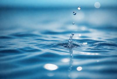 The primary subject of the image is a splash of water, which is captured in a close-up shot. The water appears to be a mix of blue and white, creating a visually appealing scene. The setting is a body of water, possibly an ocean or a lake, with a clear blue sky in the background. The visual style of the image is a close-up of the water splash, which emphasizes the details of the water droplets. The colors and mood of the image are predominantly blue,