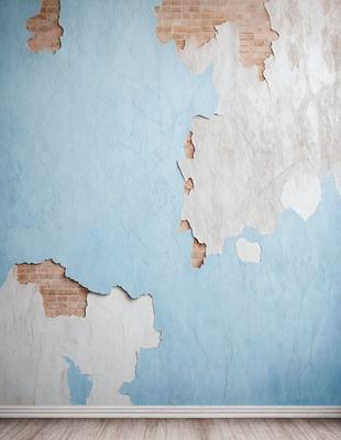 The primary subject of the image is a blue wall with peeling paint, giving it a worn and aged appearance. The setting is a room with a brick wall, which adds to the overall atmosphere. The visual style is a close-up of the wall, showcasing the peeling paint and the brick wall. The colors and mood of the image are predominantly blue, with the peeling paint adding a touch of brown and white.