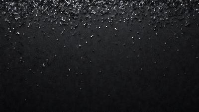 The primary subject of the image is a close-up of a black background with a pattern of white specks or glittery particles. The setting appears to be a dark room, and the visual style is a black and white photo. The dominant colors are black and white, and the overall atmosphere is somewhat mysterious or dramatic.