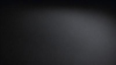 The primary subject of the image is a black background with a white light source. The setting is a dark room, and the visual style is a black and white photo. The colors and mood of the image are predominantly dark and moody, with the white light source creating a stark contrast against the black background.