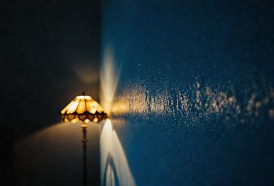 The primary subject of the image is a lamp, which is situated in a dark room. The setting is a wall, and the visual style appears to be a photo. The dominant colors in the image are blue and black, creating a moody atmosphere.