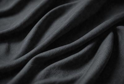 The primary subject of the image is a piece of fabric, which is the main object, scene, or focus of the image. The setting/background consists of a dark background, which contrasts with the fabric. The visual style is a close-up of the fabric, showcasing its texture and details. The colors and mood of the image are predominantly dark, with the fabric being the main source of contrast and visual interest.