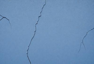 The primary subject of the image is a crack in a blue wall. The setting is indoors, with the crack being the main focus of the scene. The visual style is a close-up of the crack, which gives a sense of depth and detail. The colors in the image are predominantly blue, which creates a calm and serene atmosphere.
