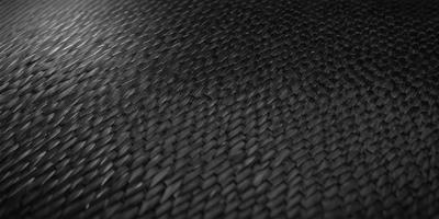The primary subject of the image is a close-up of a black, textured surface. The setting appears to be a dark room, with the surface being the main focus of the image. The visual style is a close-up of a textured surface, which gives the image a more artistic and detailed appearance. The colors in the image are predominantly black, creating a moody and dramatic atmosphere.