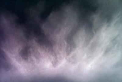 The primary subject of the image is a cloudy sky. The setting is a dark, cloudy day with a purple hue. The visual style is a photo, capturing the beauty of the cloudy sky. The colors and mood of the image are dark and moody, creating a dramatic atmosphere.