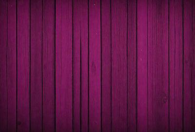 The primary subject of the image is a wooden wall with a purple color. The setting is a room with a wooden floor. The visual style is a close-up of the wooden wall, showcasing its texture and color. The dominant colors are purple and brown, creating a warm and inviting atmosphere.