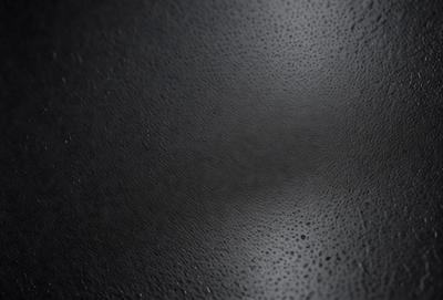 The primary subject of the image is a close-up of a black leather surface. The setting is a dark room, and the visual style appears to be a photo. The dominant colors are black and grey, creating a moody atmosphere.