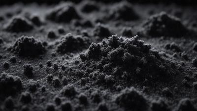 The primary subject of the image is a black substance, possibly a powder or a dark substance, with a texture that resembles a mountain. The setting is a black background, which contrasts with the black substance. The visual style appears to be a close-up of the substance, showcasing its texture and appearance. The colors and mood of the image are predominantly dark, with the black substance being the main focus.