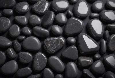 The primary subject of the image is a collection of black rocks, which are the main objects in the scene. The setting is a black background, which provides a stark contrast to the rocks. The visual style of the image is a close-up of the rocks, showcasing their unique textures and patterns. The dominant colors in the image are black and grey, creating a moody and dramatic atmosphere.