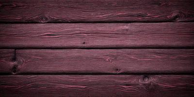The primary subject of the image is a wooden wall with a purple tint. The setting is a room with a wooden floor. The visual style is a close-up of the wooden wall, showcasing its texture and color. The dominant colors are purple and brown, creating a warm and cozy atmosphere.