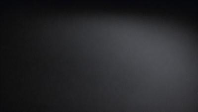 The primary subject of the image is a black background with a white light source. The setting is a dark room, and the visual style is a black and white photo. The colors and mood of the image are predominantly dark and moody, with the white light source creating a stark contrast against the black background.