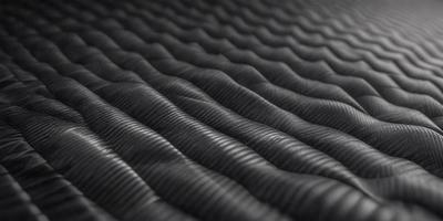The primary subject of the image is a close-up of a black, wavy surface, which appears to be a patterned fabric or a textured material. The setting is a black background, which contrasts with the wavy surface. The visual style is a close-up, focusing on the details of the wavy surface. The colors and mood of the image are predominantly black, giving it a sleek and modern appearance.