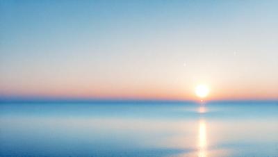 The primary subject of the image is the sunset, with the sun setting over the ocean. The setting is a vast body of water, and the visual style is a photo. The colors and mood of the image are dominated by the warm hues of the sunset, creating a serene and peaceful atmosphere.
