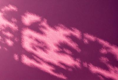 The primary subject of the image is a cloud formation in the sky. The cloud is pink and appears to be shaped like a horse. The setting is a purple sky, which adds a unique and artistic touch to the scene. The visual style of the image is a combination of photo and digital art, creating a striking and eye-catching representation of the cloud formation. The dominant colors in the image are pink and purple, giving the scene a warm and dreamy atmosphere.