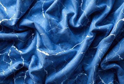 The primary subject of the image is a blue fabric with a pattern of white spots. The setting is a close-up of the fabric, showcasing its texture and design. The visual style is a detailed, up-close view of the fabric, which gives it a realistic and textured appearance. The dominant colors are blue and white, creating a calm and soothing atmosphere.