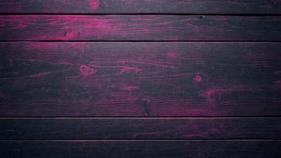The primary subject of the image is a wooden wall with a pinkish hue. The setting is a room with a wooden floor. The visual style is a close-up of the wooden wall, which gives the impression of a textured surface. The dominant colors are pink and black, creating a warm and moody atmosphere.