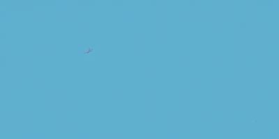 The primary subject of the image is a plane flying high in the sky. The plane is positioned towards the left side of the image. The setting is a clear blue sky, which provides a beautiful backdrop for the plane. The visual style of the image is a photo, capturing the plane in its natural environment. The colors and mood of the image are predominantly blue, creating a serene and peaceful atmosphere.