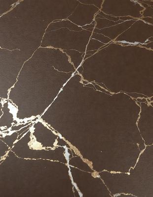 The primary subject of the image is a marble table with a gold-colored surface. The setting is a room with a brown background. The visual style is a close-up of the marble table, showcasing its unique texture and design. The colors and mood of the image are warm and elegant, with the gold and brown tones creating a sophisticated atmosphere.