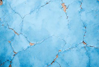 The primary subject of the image is a blue wall with a cracked and chipped surface. The setting is a room with a blue background. The visual style is a close-up of the blue wall, showcasing its texture and imperfections. The colors and mood of the image are predominantly blue, creating a calm and serene atmosphere.