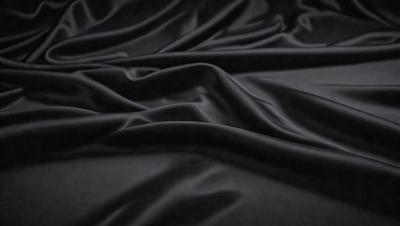 The primary subject of the image is a black fabric, which appears to be a piece of silk. The setting is a dark background, which contrasts with the black fabric. The visual style is a close-up of the fabric, showcasing its texture and details. The colors and mood of the image are predominantly dark, with the black fabric being the main focus.