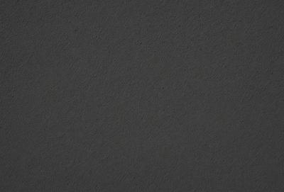 The primary subject of the image is a dark grey surface, which appears to be a leather-like material. The setting is a black background, and the visual style is a close-up of the material. The colors and mood of the image are dark and moody, with the grey surface being the dominant color.