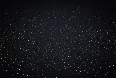 The primary subject of the image is a black background with a pattern of white dots. The setting is a dark room, and the visual style is a close-up of the dots. The colors and mood of the image are predominantly dark and moody, with the white dots providing a contrasting element.