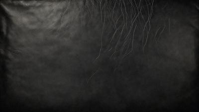The primary subject of the image is a close-up of a person's hair, which appears to be wet and possibly styled. The setting is a dark room, and the visual style is a black and white photo. The dominant colors are black and white, and the overall atmosphere is moody and dramatic.