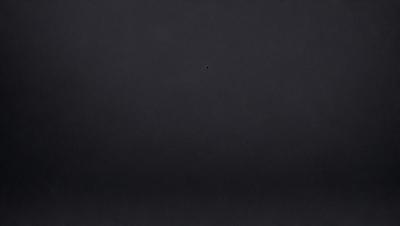 The image is a black and white photo of a dark room. The primary subject is a small dot in the center of the room, which appears to be a light source. The setting is a dark room with no other visible objects or background. The visual style is a black and white photo, giving the image a classic and timeless appearance. The colors and mood are predominantly dark and moody, with the small light source being the only bright spot in the scene.