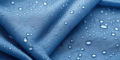 The primary subject of the image is a blue cloth with water droplets on it. The setting is a close-up of the cloth, showcasing the water droplets on its surface. The visual style is a realistic representation of the cloth with water droplets. The colors and mood of the image are predominantly blue, with the water droplets adding a touch of white and reflective quality to the scene.