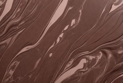 The primary subject of the image is a close-up of a brown, swirling, and textured surface, which appears to be a piece of chocolate cake. The setting is a kitchen, and the visual style is a close-up of the cake. The colors and mood of the image are warm and inviting, with the brown hues of the cake creating a sense of indulgence and comfort.
