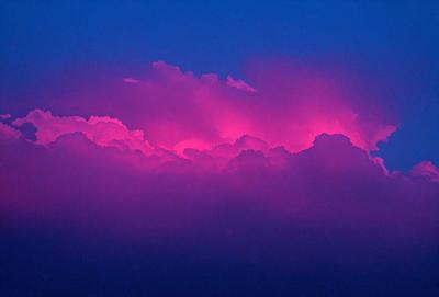 The primary subject of the image is a purple cloud in the sky. The setting is a nighttime sky, with the cloud being the main focus of the scene. The visual style appears to be a photo, capturing the purple cloud against the dark sky. The colors and mood of the image are predominantly purple, creating a serene and atmospheric scene.